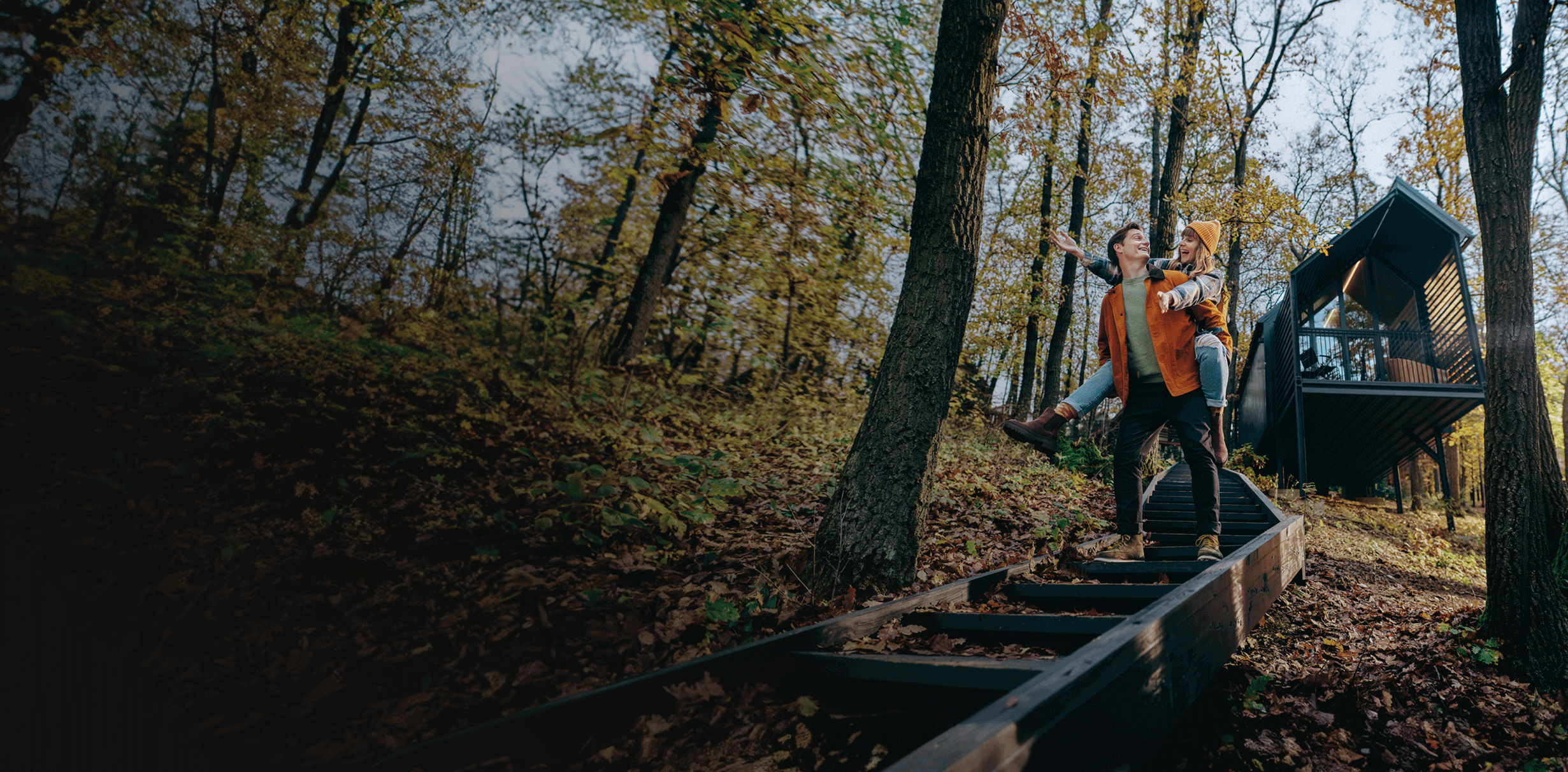 Fiatal fiú, hátán a lány, lépcsőn mennek le egy erdőben, háttérben egy házzal